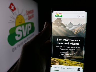 Stuttgart, Almanya - 07-28-2025: İsviçre partisi Schweizerische Volkspartei 'nin (SVP) web sayfası logonun önünde duran kişi. Telefon ekranının merkezine odaklan.