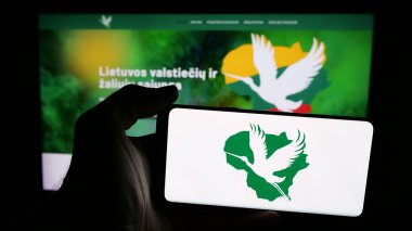 Stuttgart, Almanya - 07-28-2025: İnternet sayfası önünde Lietuvos Valstieciu ir Zaliuju Sajunga (LVZS) logosu olan cep telefonu sahibi kişi. Telefon ekranına odaklan.