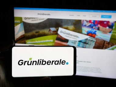 Stuttgart, Almanya - 07-30-2025: İnternet sitesi önünde üzerinde İsviçreli Gruenliberale Partei Schweiz (GLP) logosu bulunan akıllı telefon sahibi kişi. Telefon ekranına odaklan.