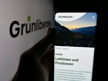 Stuttgart, Almanya - 07-30-2025: İsviçre partisi Gruenliberale Partei Schweiz 'in (GLP) web sayfası logonun önünde duran kişi. Telefon ekranının merkezine odaklan.