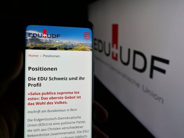 Stuttgart, Almanya - 07-30-2025: Parti Eidgenoessisch-Demokratische Union 'un (EDU) internet sayfası logonun önünde duran kişi. Telefon ekranının merkezine odaklan.