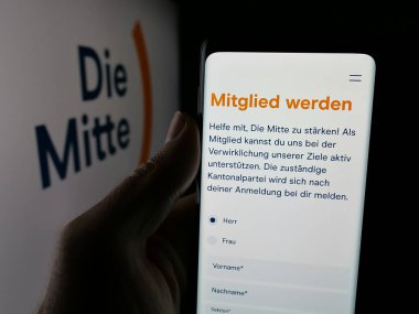 Stuttgart, Almanya - 07-30-2025: İsviçreli siyasi parti Die Mitte 'nin web sayfası logo önünde ekranda olan kişi. Telefon ekranının merkezine odaklan.