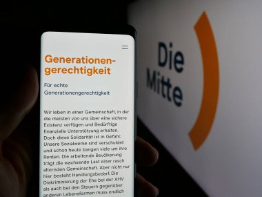 Stuttgart, Almanya - 07-30-2025: İsviçreli siyasi partinin web sitesi Die Mitte 'nin akıllı telefonunu logo önünde ekranda tutan kişi. Telefon ekranının merkezine odaklan.