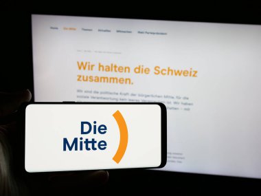 Stuttgart, Almanya - 07-30-2025: İsviçreli siyasi parti Die Mitte 'nin logosunu elinde tutan kişi web sitesi önünde ekranda. Telefon ekranına odaklan.