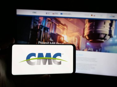 Stuttgart, Almanya - 08-14-2025: İnternet sitesi önünde ekranda ABD 'li Ticari Metaller Şirketi' nin (CMC) logosuna sahip akıllı telefon tutan kişi. Telefon ekranına odaklan.