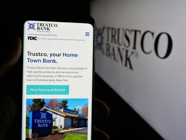 Stuttgart, Almanya - 08-18-2025: ABD 'li finans hizmetleri şirketi Trustco Bank' ın web sayfası ile akıllı telefon sahibi kişi logonun önünde ekranda. Telefon ekranının merkezine odaklan.