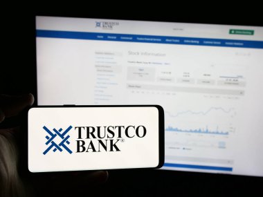 Stuttgart, Almanya - 08-18-2025: ABD 'li finans hizmetleri şirketi Trustco Bank' ın logosunu elinde tutan kişi web sitesinin önünde ekranda. Telefon ekranına odaklan.