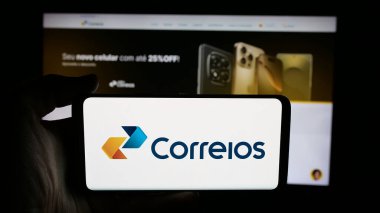 Stuttgart, Almanya - 08-19-2025: İnternet sayfası önünde ekranda Empresa Brasileira de Correios e Telegrafos logosu bulunan kişi. Telefon ekranına odaklan.