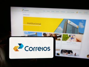 Stuttgart, Almanya - 08-19-2025: İnternet sitesinin önünde üzerinde Empresa Brasileira de Correios e Telegrafos logosu bulunan kişi. Telefon ekranına odaklan.
