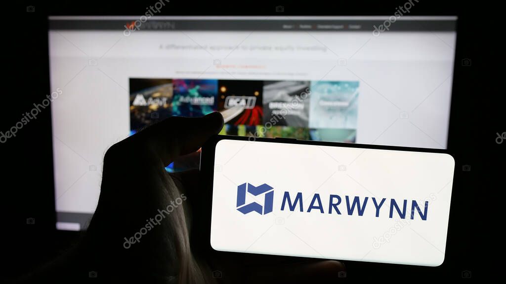 Stuttgart, Germany - 08-18-2025: Person holding mobile phone with logo of US supply chain company Marwynn Holdings Inc. on screen in front of web page. Focus on phone display.