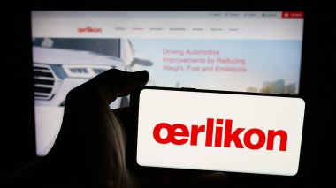 Stuttgart, Almanya - 08-20-2025: İsviçreli OC Oerlikon AG şirketinin logosuna sahip cep telefonu sahibi kişi web sayfasının önünde ekranda. Telefon ekranına odaklan.