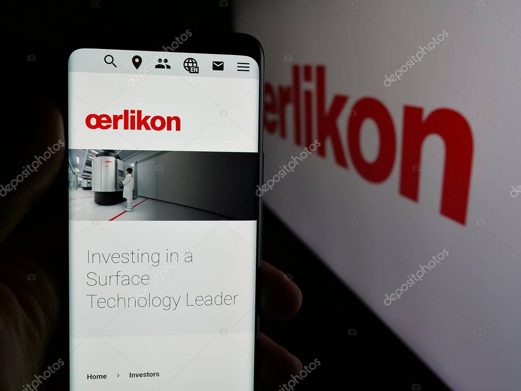 Stuttgart, Germany - 08-20-2025: Person holding smartphone with web page of Swiss company OC Oerlikon Corporation AG on screen in front of logo. Focus on center of phone display.