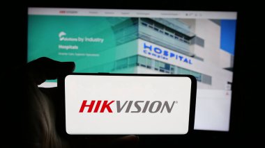 Stuttgart, Almanya - 08-22-2025: Web sayfası önünde ekranda Hangzhou Hikvision Dijital Teknoloji logosu olan kişi. Telefon ekranına odaklan.