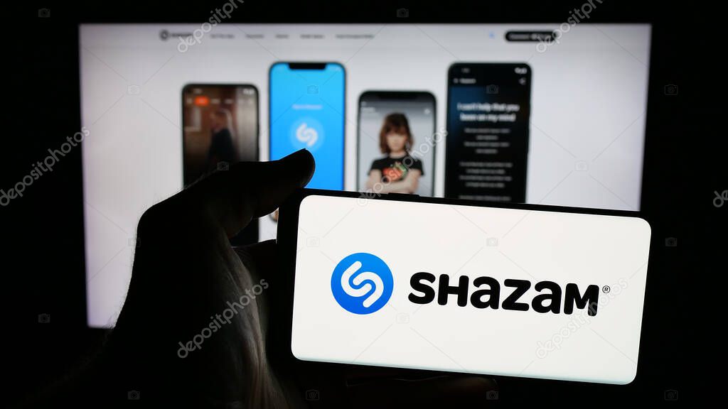 Stuttgart, Germany - 08-21-2025: Person holding mobile phone with logo of music identification app Shazam (Apple) on screen in front of web page. Focus on phone display.