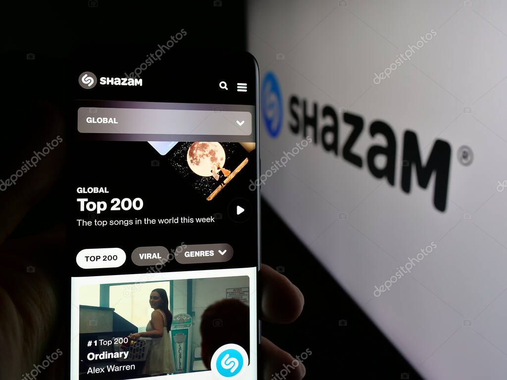 Stuttgart, Germany - 08-21-2025: Person holding cellphone with webpage of music identification app Shazam (Apple) on screen in front of logo. Focus on center of phone display.