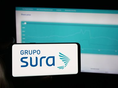 Stuttgart, Almanya - 09-27-2025: Kolombiyalı Grupo SURA şirketinin logosunun bulunduğu akıllı telefonu web sitesinin önünde elinde tutan kişi. Telefon ekranına odaklan.