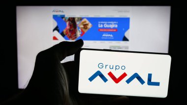 Stuttgart, Almanya - 09-29-2025: Web sayfası önünde ekranda Grupo Aval Acciones y Valores S.A. şirketinin logosuna sahip cep telefonu sahibi kişi. Telefon ekranına odaklan.