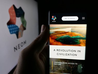 Stuttgart, Almanya - 09-29-2025: Cep telefonunda Suudi Arabistan emlak projesi NEOM 'un web sayfası bulunan kişi logonun önünde ekranda. Telefon ekranının merkezine odaklan.