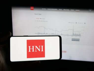 Stuttgart, Almanya - 10-04-2025: ABD 'li mobilya şirketi HNI Corporation' ın logosunu elinde tutan kişi web sitesinin önünde ekranda. Telefon ekranına odaklan.