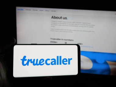 Stuttgart, Almanya - 10-04-2025: İsveçli arama şirketi Truecaller AB 'nin logosuna sahip akıllı telefon sahibi kişi web sitesinin önünde ekranda. Telefon ekranına odaklan.