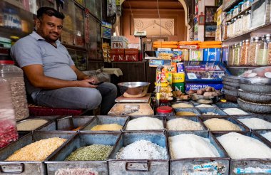 Yerli dükkan sahibi dükkanında bir dizi tahıl ve baharatla çevrili.