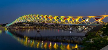 Aydınlatılmış köprü, günbatımında suya yansıyarak modern tasarımı sergiliyor.