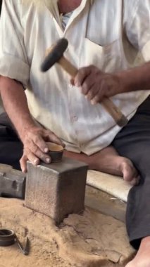 Hindistan 'da usta bir zanaatkar örsün üzerinde çekiçle bakır çan şekillendiriyor, geleneksel metal işleme tekniklerini sergiliyor.
