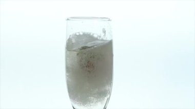 Köpüklü bir şarap kadehine düşen iki çilek beyaz arka planda ferahlatıcı bir sahne oluşturur.