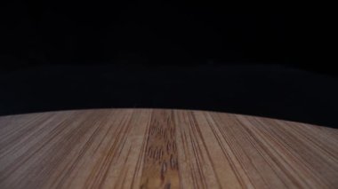 Bir bambu kesme tahtasının üzerinde süzülen kamera, parlak siyah bir arkaplan üzerine kurulmuş bir delik.