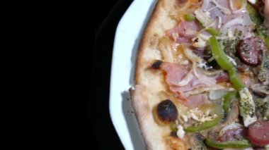 Çeşitli malzemelerle nefis bir karışım pizza siyah arka planda izole edilmiş beyaz bir tabakta dönüyor.