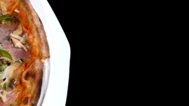 Sosisli, jambonlu ve yeşil biberli karışık pizza beyaz tabakta soldan sağa doğru kayıyor.