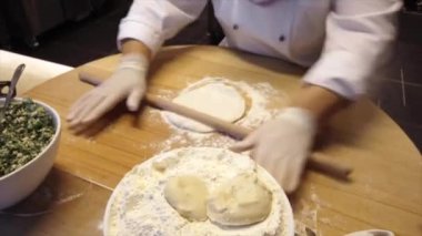 Beyaz eldiven giyen aşçı hamuru ahşap bir masaya yuvarlıyor merdaneyle, yemek hazırlama yeteneğini sergiliyor.