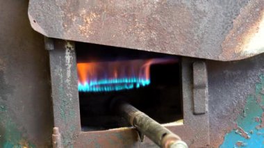 Mavi ve turuncu alevler gaz ocağından çıkar, endüstriyel mutfak ortamında kavurucu bir fırın ısıtır.