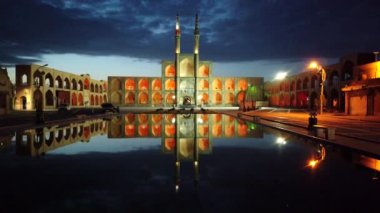 Yazd 'daki Amir Chakhmak camii alacakaranlıkta güzel bir şekilde parlıyor, yansıması suda, dramatik bir akşam gökyüzünün altında.