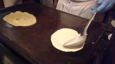 Şef, restoranın mutfağındaki bir ızgaranın üzerine hamuru döker ve yemek gibi ince bir gözleme yapar.