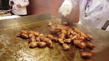 Beyaz önlüklü ve eldivenli şefler ızgarada tavuk pişirir. Mutfakta aşçılık yetenekleri sergilerler.