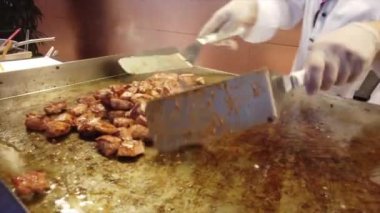 Şef ızgarada küçük bir parça tavuk pişiriyor, onları spatulayla ustalıkla pişiriyor.