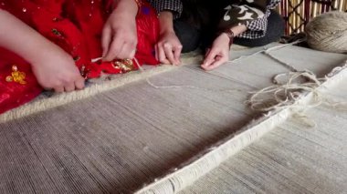 İki kadın halıya oturmuş, halıyı ustalıkla örüyorlar. Elleri ve küçük aletleriyle.
