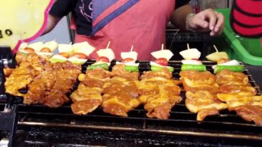 Sokak yemekleri satıcısı ızgarada tavuk şişi pişirirken barbekü sosu pişiriyor.