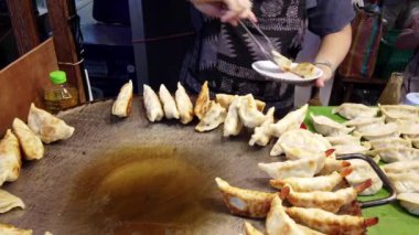 Gyoza servis eden sokak yemekleri satıcısı, ızgaradan çıkan hamur köftelerini bekleyen bir müşteriye servis etmek için maşa kullanır.