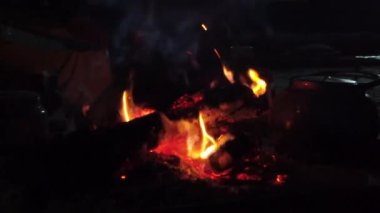 Alevler yanan odunlar üzerinde dans eder, karanlık bir çöl gecesinin arka planında tencereleri aydınlatır. Sıcaklık dinginlikte parlıyor.