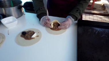 Eldiven giyen bir sokak satıcısı et ve sebze dolgusu üzerine tortilla katlıyor.