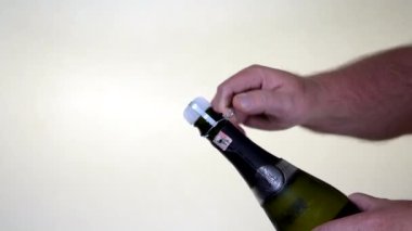 Sommelier şampanya şişesinden beyaz arka plana doğru tel kafesi çıkarır ve süreci ayrıntılı bir şekilde gösterir.