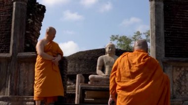 Turuncu cübbe giyen Budist rahipler Polonnaruwa, Sri Lanka 'daki bir tapınağın Buda heykelinin yanından yukarı çıkıyorlar.