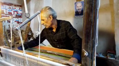 İsfahan 'daki yaşlı zanaatkar, İran titizlikle el dokuması kullanarak geleneksel bir aliaqa pelerini örüyor.