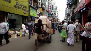 Teslimatçı, Colombo, Sri Lanka 'daki kalabalık bir caddede içi karton kutularla dolu büyük bir el arabasını çekmeye çalışıyor.