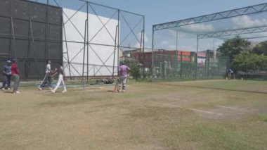 Genç kriket oyuncusu açık hava eğitim tesisinde vuruş antrenmanı yapıyor. Antrenman sırasında yetenek ve konsantrasyon sergiliyor.