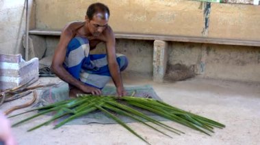 Palmiye yaprakları ören bir zanaatkar tropik bir ortamda yetenek ve konsantrasyonla geleneksel çatı malzemesi yaratır.