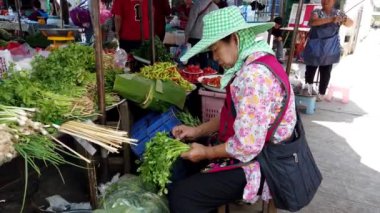 Chiang Saen, Tayland 'daki hareketli bir markette maydanoz kesen şapkalı bir satıcı yerel ürünleri sergiliyor.