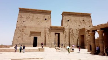 Güneşli bir gökyüzü altında antik filae tapınağı kompleksinde yürüyen turistler çarpıcı mimariye ve tarihe hayran kalıyorlar.